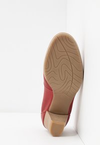 Czerwona skórzana shoe z teksturowaną, tanową gumową podeszwą. Podeszwa ma falisty wzór, a but posiada podwyższone obcasy dla dodatkowego wsparcia.