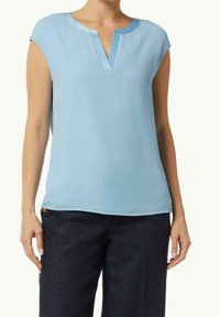 Blusa azzurra chiara a maniche corte con scollo a V e una texture morbida. Indossata con pantaloni in denim scuro caratterizzati da un semplice bottone decorativo.