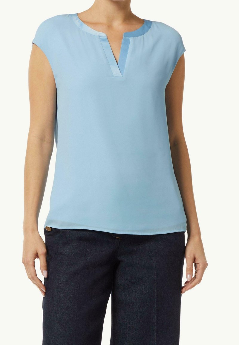 Blusa azzurra chiara a maniche corte con scollo a V e una texture morbida. Indossata con pantaloni in denim scuro caratterizzati da un semplice bottone decorativo.