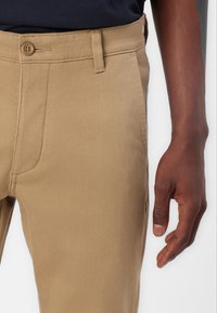 Beige chinos made of cotton blend, featuring a straight cut, button closure, and side pockets, with visible stitching and a smooth texture.