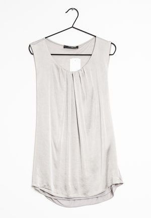 Blusa sin mangas de color gris claro con pliegues en el escote, colgada en una percha negra sobre un fondo blanco.