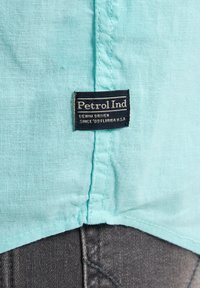 Camicia in tessuto azzurro chiaro con finitura testurizzata, caratterizzata da un'etichetta nera con la scritta "Petrol Ind" e cuciture a contrasto.