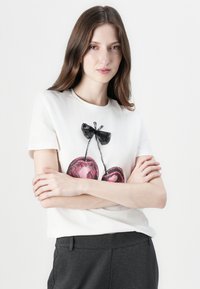 Cotton t-shirt i off-white med en illustration af to pink kirsebær med en sort sløjfe ovenfor, rund halsudskæring og korte ærmer.