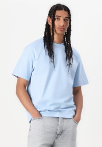 Lyseblå bomuld t-shirt med korte ærmer, rund halsudskæring og afslappet pasform. Let slidte detaljer er synlige på sømmene.