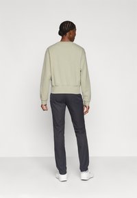 Gaiši zaļš sweatshirt ar ribotām aprocēm un apakšmalu, apvienots ar tumši pelēkām biksēm, radot gadījuma stila izskatu. Fons ir vienkārši balts.