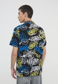 Camicia a maniche corte con sfondo nero e vivaci motivi di graffiti bianchi, blu e giallo neon; vestibilità rilassata; morbido tessuto.