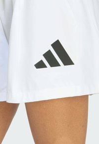 Bijele sportske kratke hlače sa glatkom teksturom i Adidasovim crnim logotipom s tri dijagonalne pruge na lijevoj strani.
