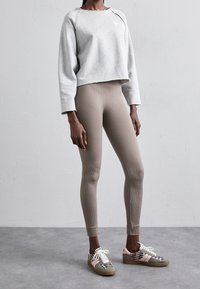 Sweatshirt court gris clair avec des leggings beiges à côtes et des baskets à motifs avec des accents roses et marron. Textures lisses et côtelées.