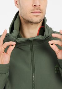 Grøn zip-op jakke med høj krave, elastiske manchetter, indre fleece-foring og justerbare funktioner for en tætsiddende pasform.
