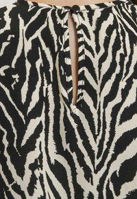 Tissu à rayures noires et blanches en forme de zèbre avec un détail d'encolure en trou de serrure, doté d'une fermeture à bouton dans le dos. Texture lisse, design décontracté.