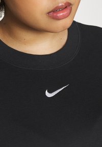 Černá mikina s kulatým výstřihem, měkkou texturou, s bílým logem Nike Swoosh na přední straně. Ležérní, minimalistický design.