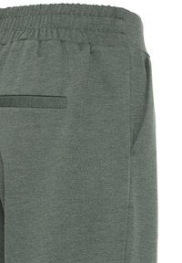 Pantaloni de trening verzi, texturați, cu un brâu moale, buzunare laterale și dungi orizontale subtile. Materialul pare elastic și confortabil.