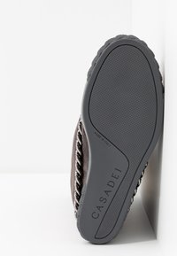 Semelle d'une chaussure Casadei avec une semelle en caoutchouc texturée, la marque "Made in Italy" et un détail de chaîne argentée sur le côté.