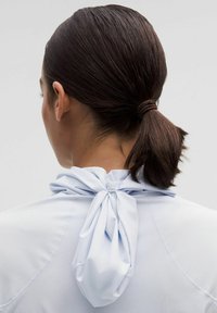 Light blue sports top with a gathered tie detail at the neck, featuring smooth, stretchy fabric and flat seams for comfort and flexibility.