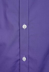 Nahaufnahme eines violetten Hemdvorderteils mit weißen Knöpfen und sichtbaren Nähten entlang der Knopfleiste.