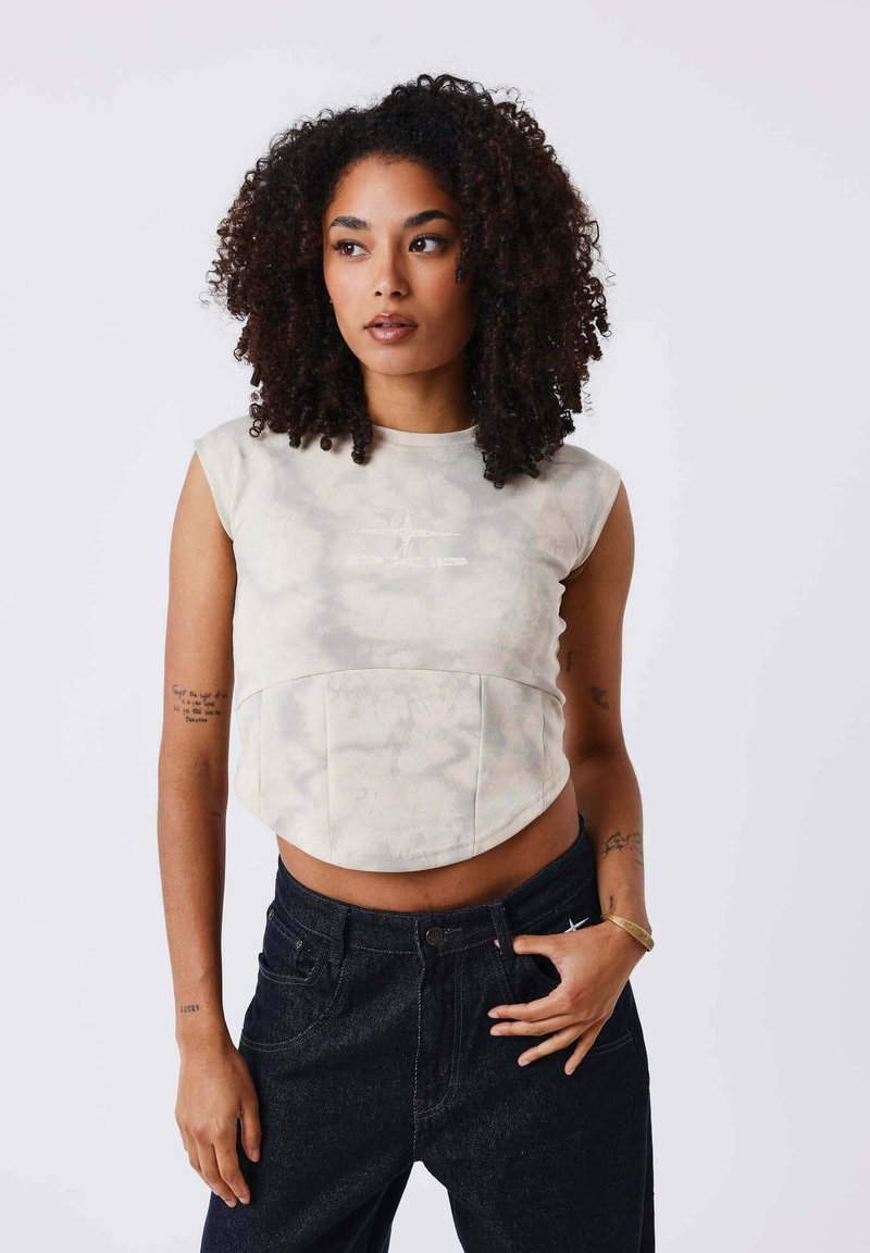 Top court sans manches dans un motif tie-dye beige clair avec un design arrondi et un panneau avant, associé à un jean foncé taille haute.