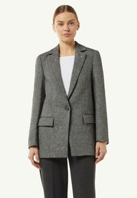 Szary blazer w wzór jodełki z klapami w kształcie notcha, z jednym guzikiem i dwoma przednimi kieszeniami. Połączony z gładką, białą koszulą.