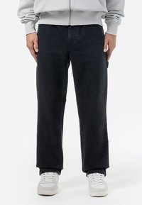 Sorte denimbukser med lige ben-design. Har et tekstureret stof og sidelommer, parret med hvide sneakers.