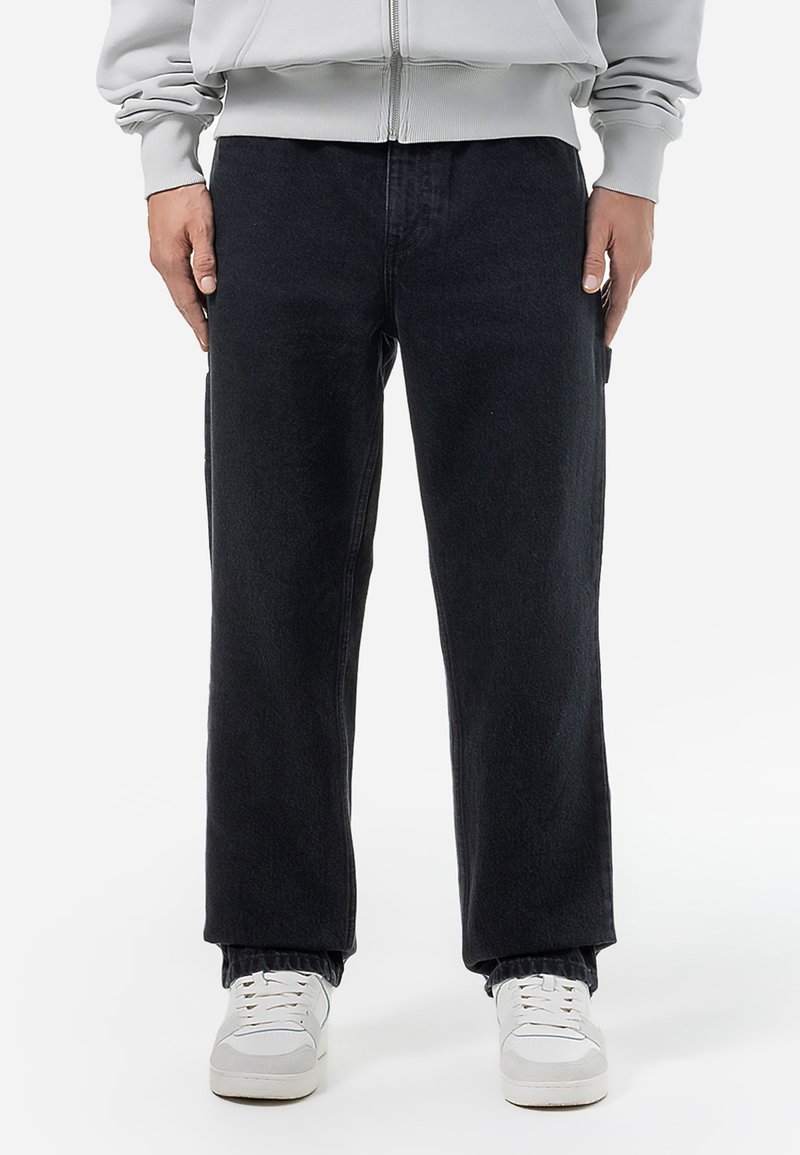 Sorte denimbukser med lige ben-design. Har et tekstureret stof og sidelommer, parret med hvide sneakers.