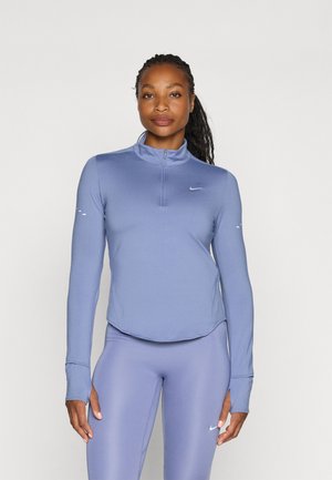 Langermet, lyseblå treningspullover med halv-glidelås i kragen. Har et Nike-logo på brystet og tommelhull i mansjettene.