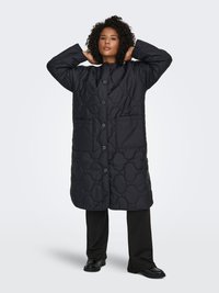 Melns ilgs šūts mētelis ar apaļu apkakli, divām priekšējām kabatām un pogu aizdari. Raksturots ar reljefu rakstu un vaļēju piegriezumu.