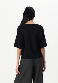 Top de punto negro de gran tamaño con mangas cortas, escote redondeado y dobladillo acanalado. Combinado con pantalones de pierna ancha grises.