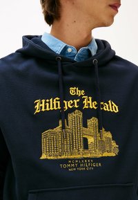 Marineblauer Hoodie mit gelbem, gesticktem Stadtbild-Design. Kapuze mit Kordelzug, Kängurutasche und sichtbarer, geschichteter Denim-Hemdkragen.