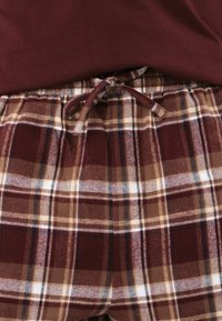 Mjuk, vinröd pyjamasöverdel med rutiga byxor i brunt, beige och vitt, med elastiskt midjeband och snöre för justerbar passform.