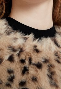 Eläinkuosilla varustettu tekoturkistoppi, jossa on musta ribbireuna. Tekstuuri on pehmeä ja sävyjä on vaihteleva ruskean ja tummanruskean välillä.