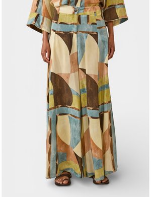 Pantaloni a gamba larga con motivo geometrico astratto in beige, marrone, blu e verde, abbinati a top coordinato e sandali marroni.