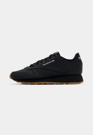 Black athletic shoes with a sleek design, featuring a textured upper, rubber sole, Reebok logo, and contrasting gum outsole.