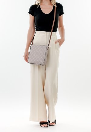 Sac bandoulière gris avec motif losange, sangle marron, forme rectangulaire. Le modèle porte un haut noir et un pantalon large crème. Sandales noires.