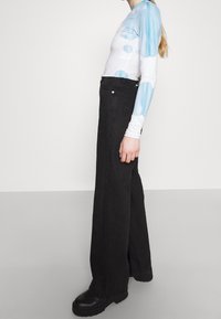 Top ajustado de manga larga con puntos de acuarela azul, combinado con jeans negros de pierna ancha de cintura alta y botas de plataforma negras chunky.