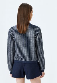 Marinblå stickad tröja med vita vertikala ränder, texturerad tyg, rund halsringning och ribbade muddar, parat med matchande marinblå shorts.