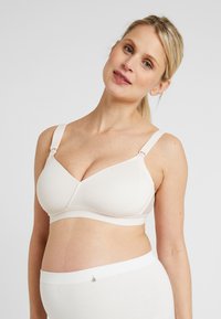 Lichtbeige zwangerschapsbh met zachte, naadloze cups en verstelbare schouderbandjes. Beschikt over delicate kantafwerking en een haaksluiting voor ondersteuning.