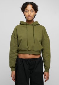 Olive green cropped hoodie with a drawstring hood, dropped shoulders, and soft texture. Paired with black elastic waistband pants.