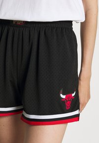 Henkilö, jolla on päällään mustat verkkosukkahousut, joissa on punaiset, valkoiset ja mustat viikset, sekä punainen härkälogo vasemmalla lahkeella.