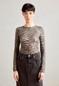 Langärmliges, transparentes Oberteil mit einem Zebramuster in Beige und Schwarz, kombiniert mit einem dunkelblauen Jeansrock mit vorderen Knöpfen und Taschen.