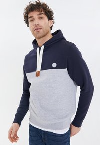 Navyblaue und graue Kapuzenjacke mit weißem Kordelzug und Lederakzenten. Verfügt über ein rundes Logo auf der oberen linken Brust.