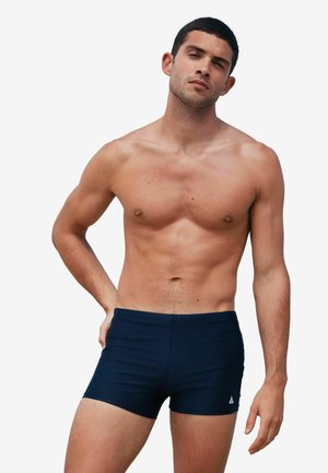 Navy swim shorts made of lightweight, stretchy fabric, featuring a snug fit and a small logo on the front left side.