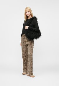 Sort faux fur håndtaske med en tekstureret, shaggy overflade. Parret med brune leopardtryk brede benbukser og en sort langærmet bluse.