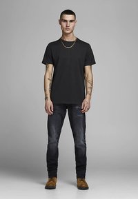Svart bomull t-skjorte med korte ermer, kombinert med mørkeblå denimjeans. Modellen har på seg brune sko og et gullkjede.