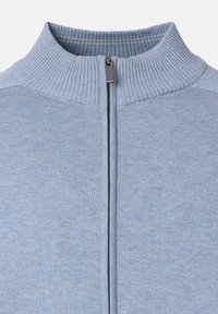 Ljusblå zip-up tröja med hög krage, ribbad textur och silverfärgad dragkedja, med en liten logotyp i nedre högra hörnet.