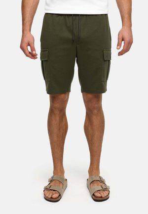 Mand iført olivengrønne cargoshorts med sidelommer og beige sandal med spænde, stående mod en hvid baggrund.