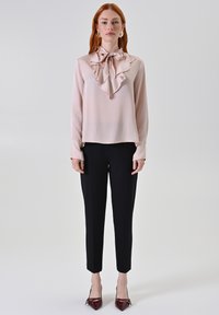 Helles rosa Blusenshirt mit Rüschensaum, kombiniert mit schwarzen, taillierten Hosen und spitzen burgunderfarbenen Pumps. Glattes Material, lange Ärmel und klassischer Schnitt.