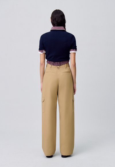 Polo in maglia blu navy con colletto abbinato a pantaloni cargo a gamba larga beige, caratterizzati da tasche laterali e chiusura con bottone in vita.