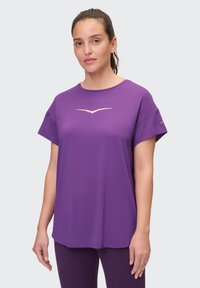 Lila Sport-T-Shirt aus glattem Stoff, mit einem goldenen Logo auf der Vorderseite und kurzen, lässig sitzenden Ärmeln.