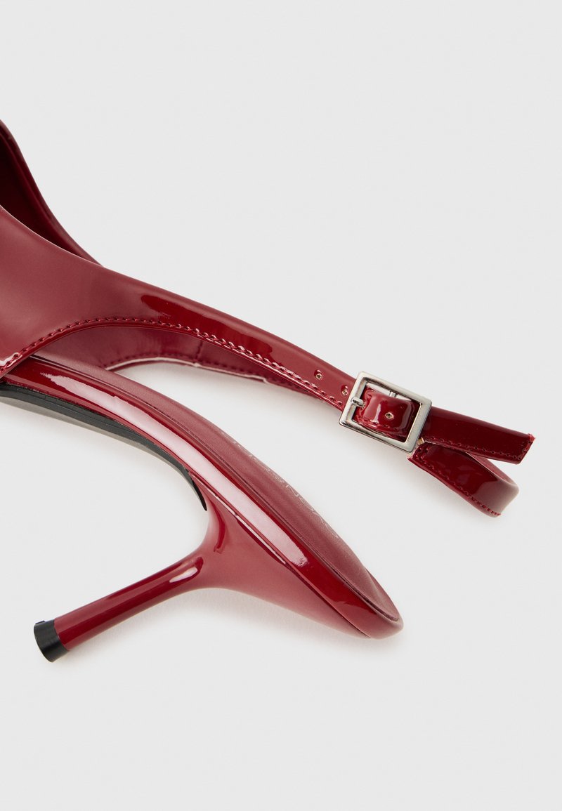 Scarpe con tacco alto in pelle verniciata rossa, con punta appuntita, dotate di cinturino alla caviglia e fibbia argentata. Finitura liscia e silhouette elegante.