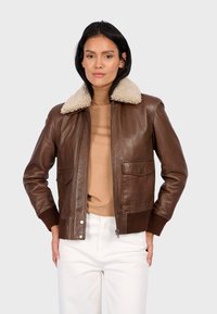 Chaqueta bomber de cuero marrón con un cuello de borrego color beige, cierre de cremallera y dos bolsillos frontales. Puños y dobladillo acanalados. Textura suave.