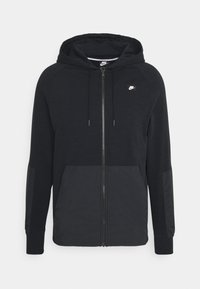 Svart huvtröja med dragkedja, tillverkad av ett strukturerat tyg. Har sidopaneler och en liten Nike-logotyp på bröstet.